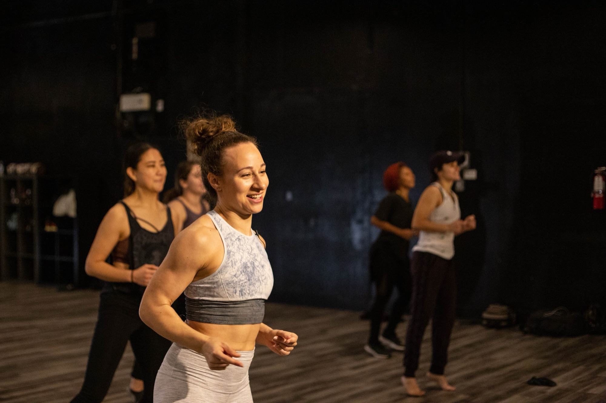 Galit grinning mid count at the front of a conditioning class at Movement Lifestyle, the group behind her