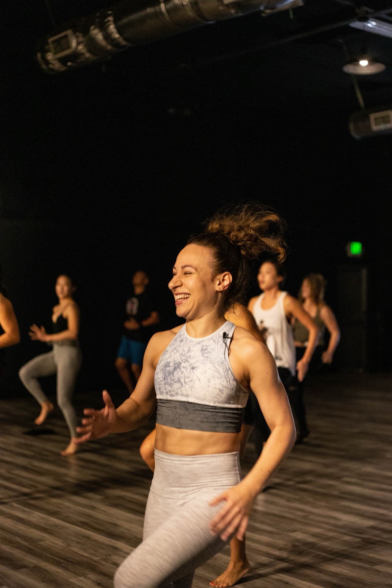 Galit laughing at the front of a class at Movement Lifestyle, the room moving behind her
