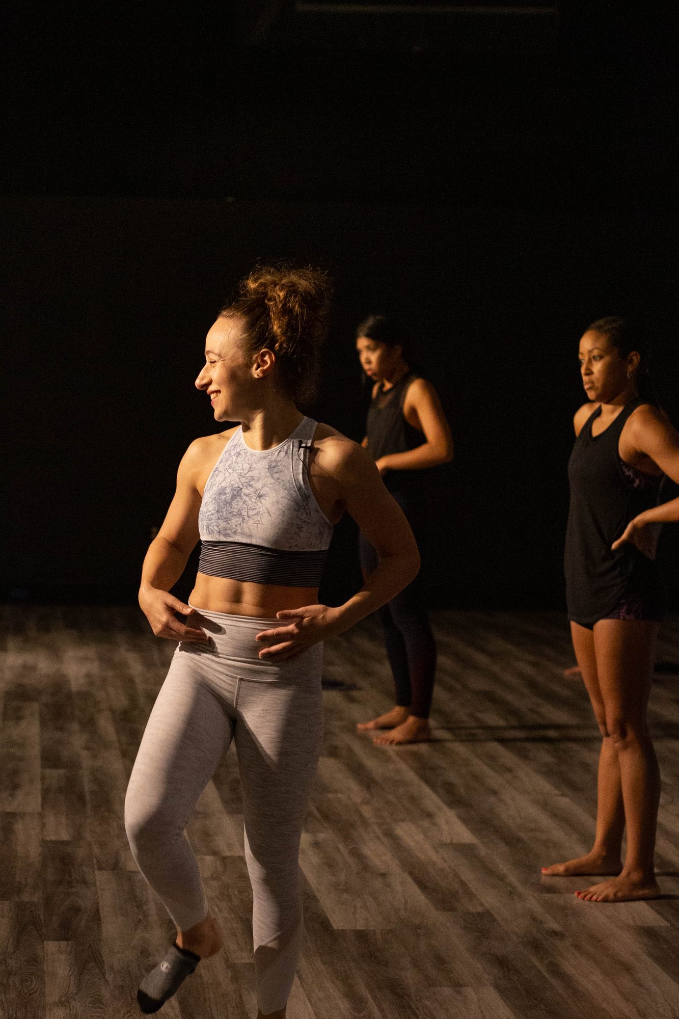 Galit smiling mid class in a dark studio, two students standing beside her