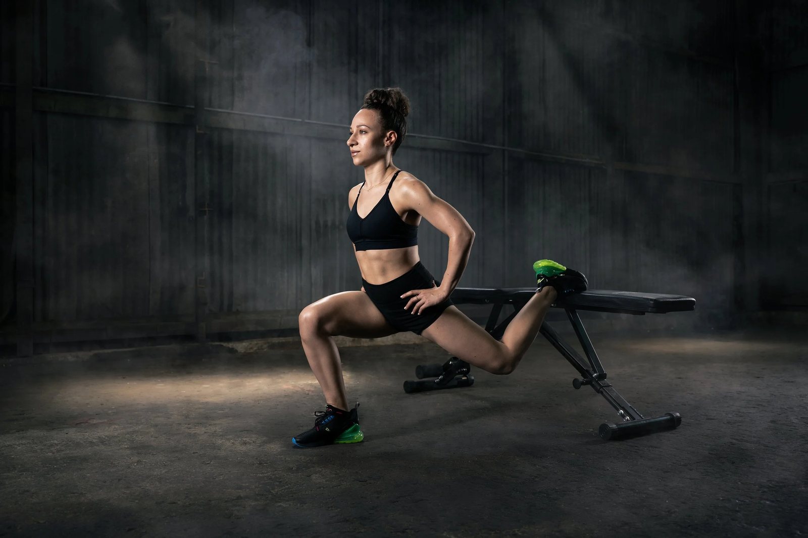 Galit Friedlander holding a split lunge off a bench in a dark warehouse