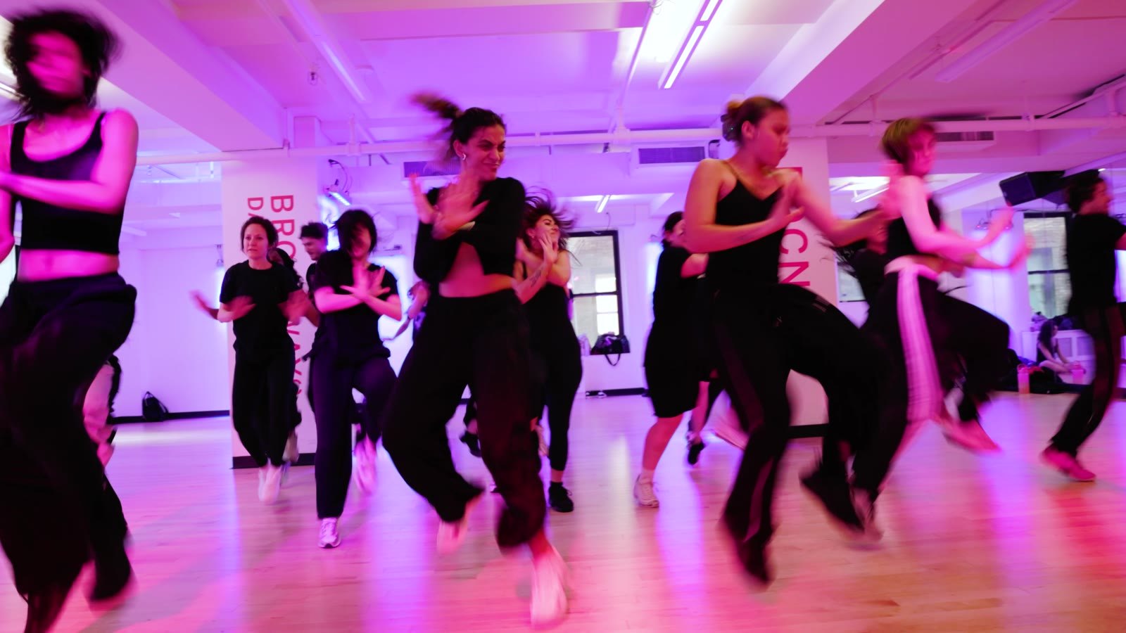 A full class moving together at Broadway Dance Center under magenta light