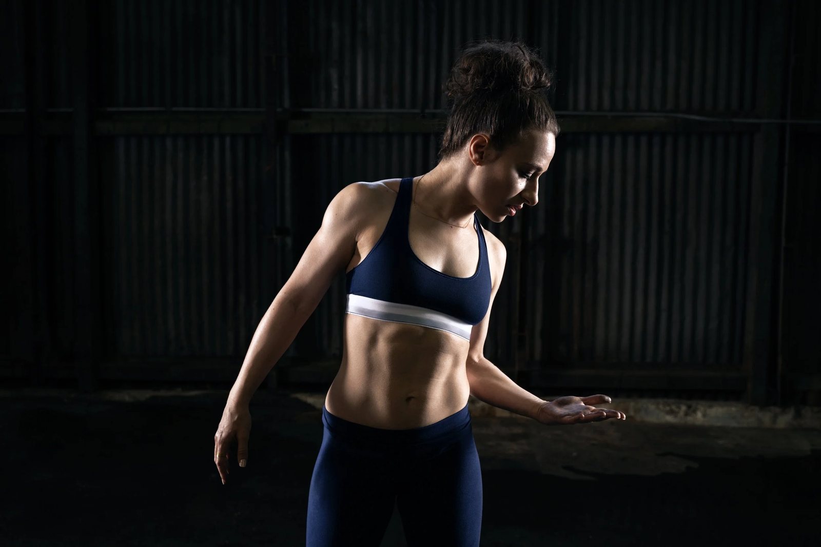 Galit standing in a dark warehouse in training gear, lit from one side
